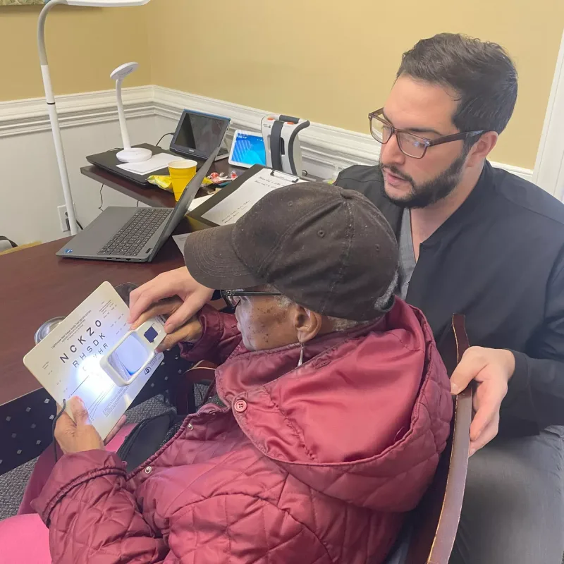 An assistant helping an elderly woman read with a magnifying glass